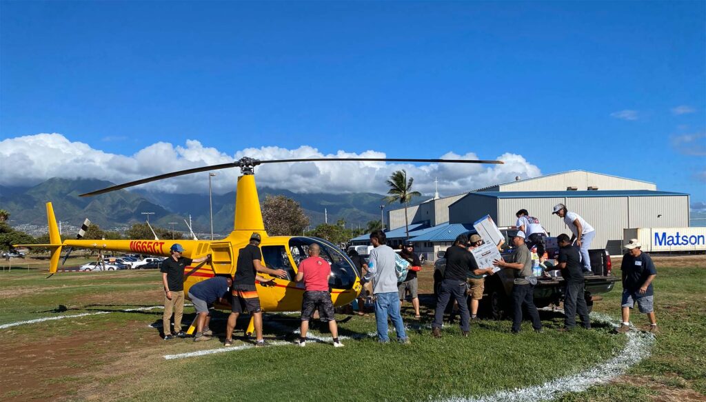 A line of people move supplies from a parked helicopter to a waiting pickup truck
